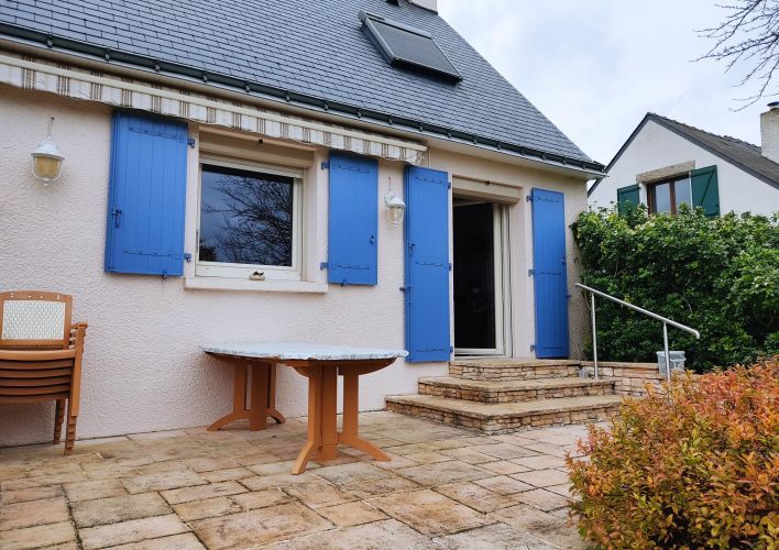 6746d82405976 Une charmante terrasse en pierre donnant sur une maison avec des volets bleus et un toit en ardoise, entourée de végétation.