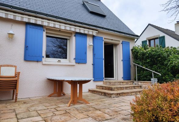 6746d82405976 Une charmante terrasse en pierre donnant sur une maison avec des volets bleus et un toit en ardoise, entourée de végétation.