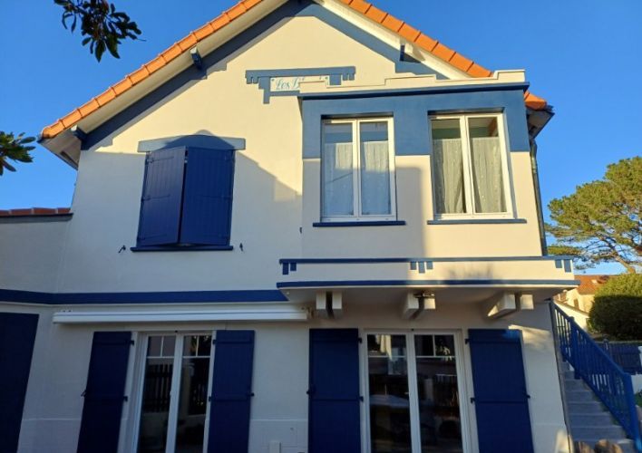 6746e2081ead6 Façade d'une maison traditionnelle avec volets et cadres de fenêtres bleus, illuminée par le soleil.