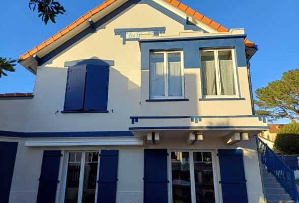 6746e2081ead6 Façade d'une maison traditionnelle avec volets et cadres de fenêtres bleus, illuminée par le soleil.