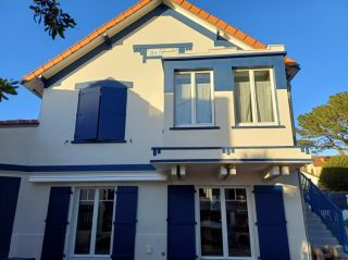 Façade d'une maison traditionnelle avec volets et cadres de fenêtres bleus, illuminée par le soleil.