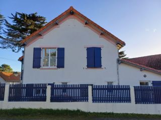 6746e20a8c880 Maison traditionnelle avec volets bleus et toit en tuiles, entourée d'une clôture en bois, sous un ciel dégagé.