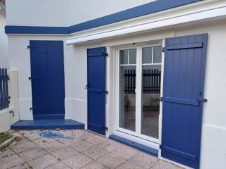 6746e20c6c28a Façade de maison avec des volets bleus et une porte-fenêtre donnant sur une terrasse en pierre.