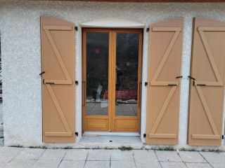 Une porte en bois avec des volets fermés sur une façade en crépi clair.