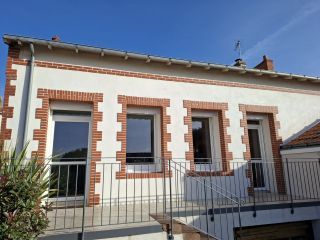 Façade d'une maison avec des encadrements en briques rouges contre un crépi blanc sous un ciel bleu.