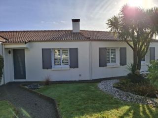 Maison de plain-pied au style méditerranéen avec toit en tuiles, volets gris et jardin orné de palmiers.