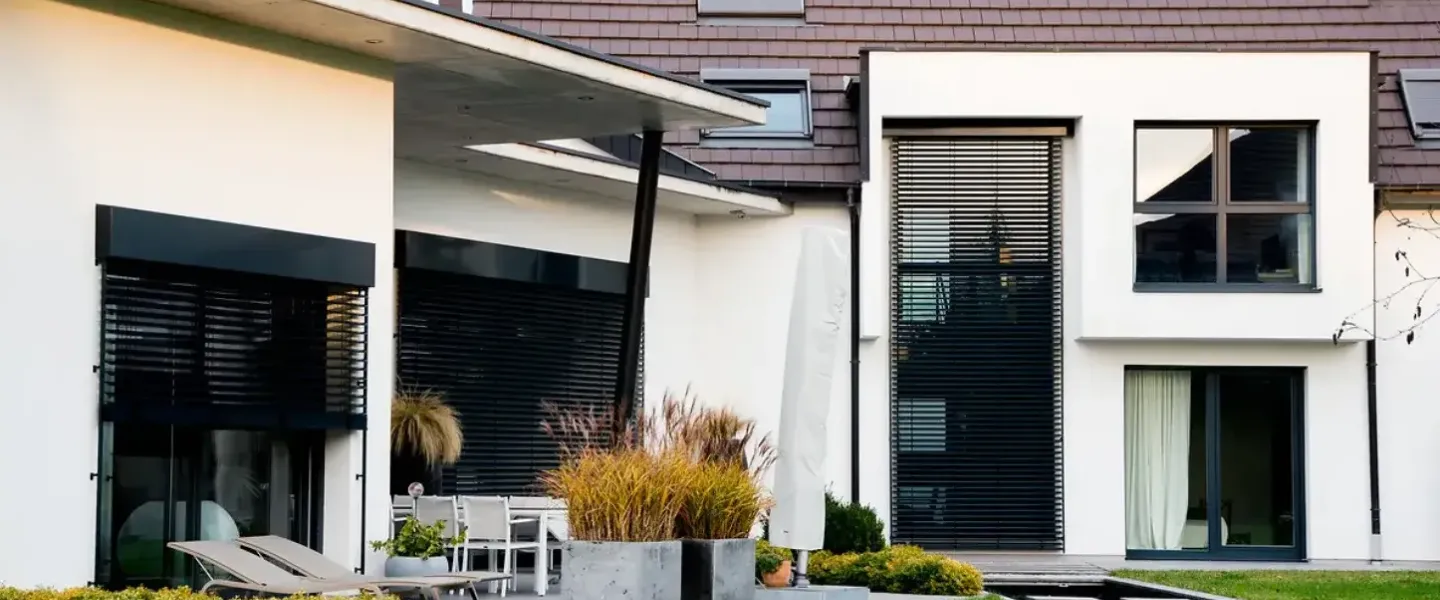 TRYBA portes fenêtres aluminium Une maison moderne avec une façade blanche et un toit en tuiles brunes, entourée d'un jardin bien entretenu.