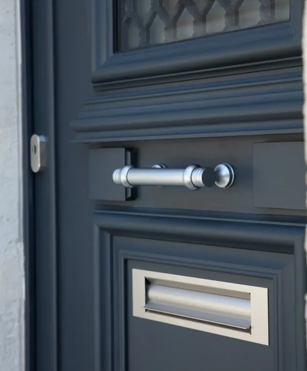 Gros plan sur une porte moderne en métal gris foncé avec une poignée chromée élégante et une boîte aux lettres intégrée.