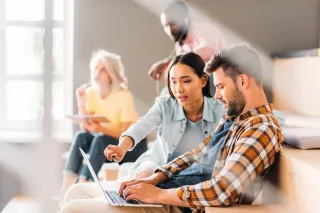 AdobeStock_210831000.webp Un groupe de jeunes adultes collaborent sur un projet, avec deux d'entre eux travaillant ensemble sur un ordinateur portable.