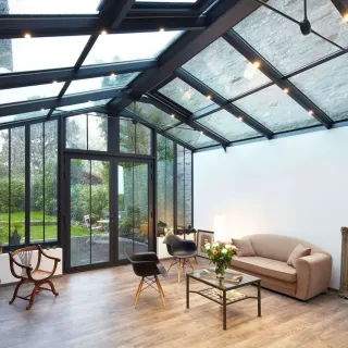 chauffer_veranda.webp Une véranda moderne avec toit en verre et mobilier élégant, offrant une vue sur un jardin verdoyant.