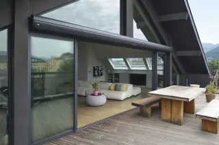 choisir_des_volets_roulants_1.webp Une terrasse en bois moderne avec de grandes portes vitrées donnant sur un salon lumineux et spacieux.
