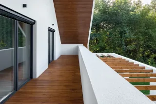 choisir_TRYBA_volets_roulants.webp Une terrasse moderne en bois avec des garde-corps blancs et vue sur la verdure environnante.