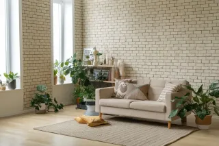 Coefficient_Uw.webp Salon moderne avec un canapé beige, plantes vertes et mur en briques blanches.