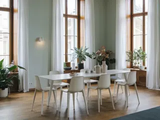 Double_ou_triple_vitrage_isolation_phonique.webp Une salle à manger lumineuse avec une grande table blanche entourée de chaises, baignée de lumière naturelle par de grandes fenêtres et agrémentée