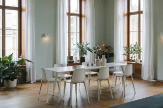 Double_ou_triple_vitrage_isolation_phonique.webp Une salle à manger lumineuse avec une grande table blanche entourée de chaises, baignée de lumière naturelle par de grandes fenêtres et agrémentée