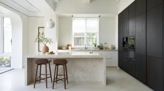 Double_ou_triple_vitrage.webp Une cuisine moderne et lumineuse avec un îlot central en pierre, des armoires sombres et deux tabourets en bois, offrant une ambiance