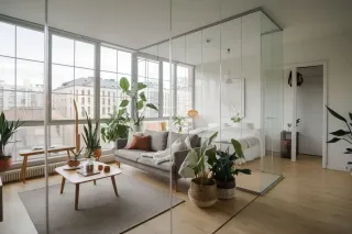 double_ou_triple_vitrage.webp Un salon moderne et lumineux avec des plantes vertes et une cloison en verre séparant l'espace chambre.
