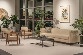 double_vitrage_durable.webp Un salon élégant et moderne avec un canapé beige, deux fauteuils assortis, une table basse noire et plusieurs plantes vertes, baigné de lumière