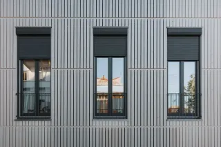 economie_volet.webp Façade moderne avec trois fenêtres alignées sur un revêtement extérieur à rayures verticales grises.