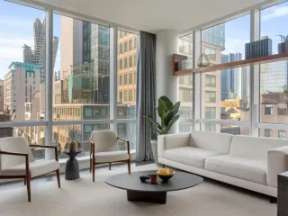 Un salon moderne et lumineux avec de grandes fenêtres offrant une vue sur la ville, décoré avec des meubles minimalistes et des plantes vertes.