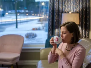 Une femme confortable assise dans un salon, dégustant une boisson chaude face à une fenêtre donnant sur un paysage hivernal.