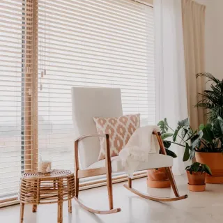 fenetre_securite_double_ou_triple_vitrage.webp Un fauteuil à bascule blanc avec un coussin à motifs géométriques se trouve près d'une fenêtre ensoleillée, entouré de plantes en