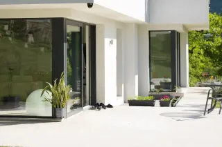 fenetre_style_maison_couleur.webp Terrasse moderne et épurée avec de grandes fenêtres et des plantes en pot, offrant une vue lumineuse sur l'extérieur.