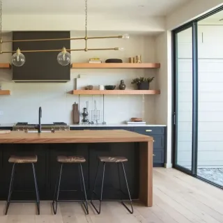 fenetre_triple_vitrage_installation.webp Une cuisine moderne avec un îlot central en bois, des tabourets design, des étagères murales et un éclairage élégant.