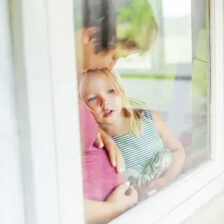 fenetre_verre_trempe.webp Deux enfants regardent pensivement par une fenêtre, l'aîné serrant tendrement le plus jeune contre lui.