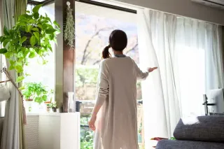 fonctionnement_ventilation_absportion_acoustique.webp Une femme, de dos, ouvre les rideaux de sa maison entourée de plantes verdoyantes et baignées de lumière naturelle.