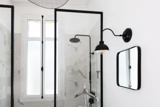 grille_hydrorgrable_avantage.webp Salle de bain moderne avec douche à l'italienne, parois en verre et éclairage mural noir.