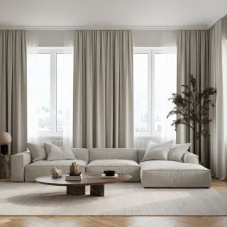 infiltration_d'air_fenetre.webp Un salon lumineux et moderne avec un canapé beige, une table basse en bois et de grandes fenêtres encadrées de rideaux clairs.