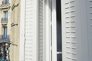 Isolation_phonique_des_volets.webp Vue sur un balcon parisien avec des volets blancs ouverts laissant entrer la lumière.