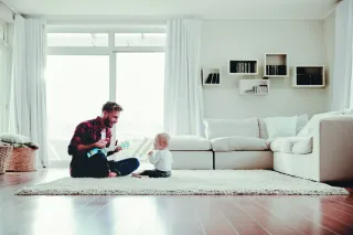 iStock-947844622-1-2.webp Un père jouant de la guitare pour son enfant dans un salon lumineux et moderne.