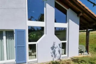 maison_suisse.webp Façade d'une maison moderne avec de grandes fenêtres en forme de bouteille, offrant une vue sur un environnement verdoyant.