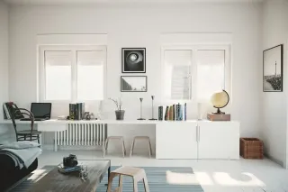 matriaux_volets.webp Un bureau moderne et minimaliste avec un grand plan de travail blanc, des étagères remplies de livres, et des fenêtres laissant entrer la lumière