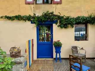 Une porte bleue entourée de lierre, avec des éléments colorés et des fleurs, décore la façade en stuc jaune d'une maison
