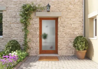 Entrée de maison charmante avec porte en bois vitrée et mur en pierres, entourée de plantes vertes et de fleurs colorées.