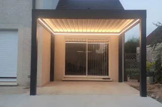 pergola_eclairage.webp Une pergola moderne avec éclairage intégré se tenant devant une baie vitrée.