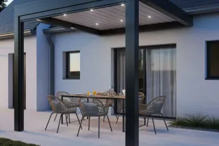 pergola_saisons.webp Terrasse moderne avec un toit en pergola illuminé et un ensemble de meubles en rotin autour d'une table dressée.