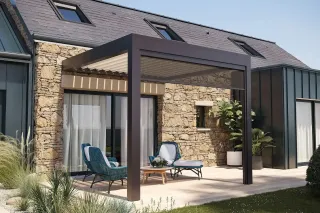 personnalisation_pergola_pure_line.webp Une terrasse moderne avec pergola bioclimatique, adossée à une maison en pierre, aménagée de chaises en osier et entour
