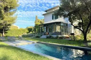 personnalisation_veranda.webp Grande maison blanche avec véranda, entourée d'un jardin verdoyant et d'une piscine moderne.
