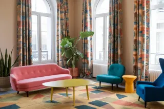pont_thermique_salon.webp Un salon coloré avec des meubles modernes, comprenant un canapé rose, des fauteuils bleus, et une table basse jaune, entouré de ride