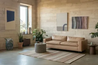 prix_fenetre_double_vitrage.webp Le salon élégant et minimaliste présente un canapé en cuir beige, des plantes vertes, des œuvres d'art modernes, et une luminosité naturelle.