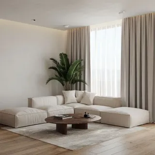 rideau_thermique_fenetres_salon.webp Un salon lumineux et minimaliste avec un canapé blanc en forme de L, une table basse ronde en bois et une plante d'intérieur, baigné de