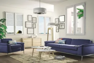 securite_volets.webp Un salon moderne et lumineux avec des murs blancs, un canapé bleu, des coussins colorés et un mobilier en bois clair, agrémenté de