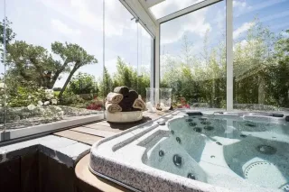 sur_mesure_veranda.webp Un jacuzzi luxueux est installé dans une véranda lumineuse avec vue sur le jardin.