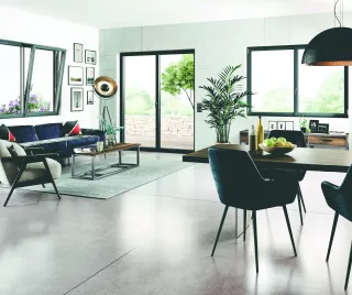 TA76oc_SALLE_a_MANGER.webp Un salon moderne et lumineux avec une décoration épurée, un canapé bleu, des fenêtres et portes vitrées donnant sur un espace extérieur verdoyant.