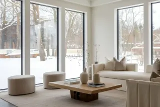 Triple_vitrage_climats_froids.webp Un salon moderne et minimaliste avec de grandes fenêtres offrant une vue sur un paysage enneigé.
