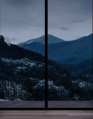 Vue nocturne sur des montagnes enneigées depuis une large baie vitrée, offrant une ambiance calme et sereine.